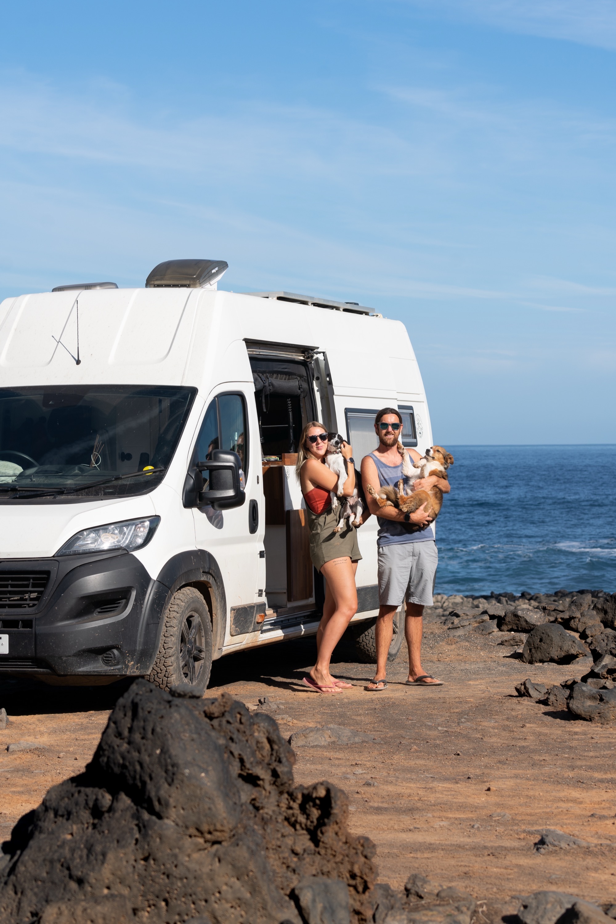 Jess and Marcus with the dogs outside the van on a rocky coastline