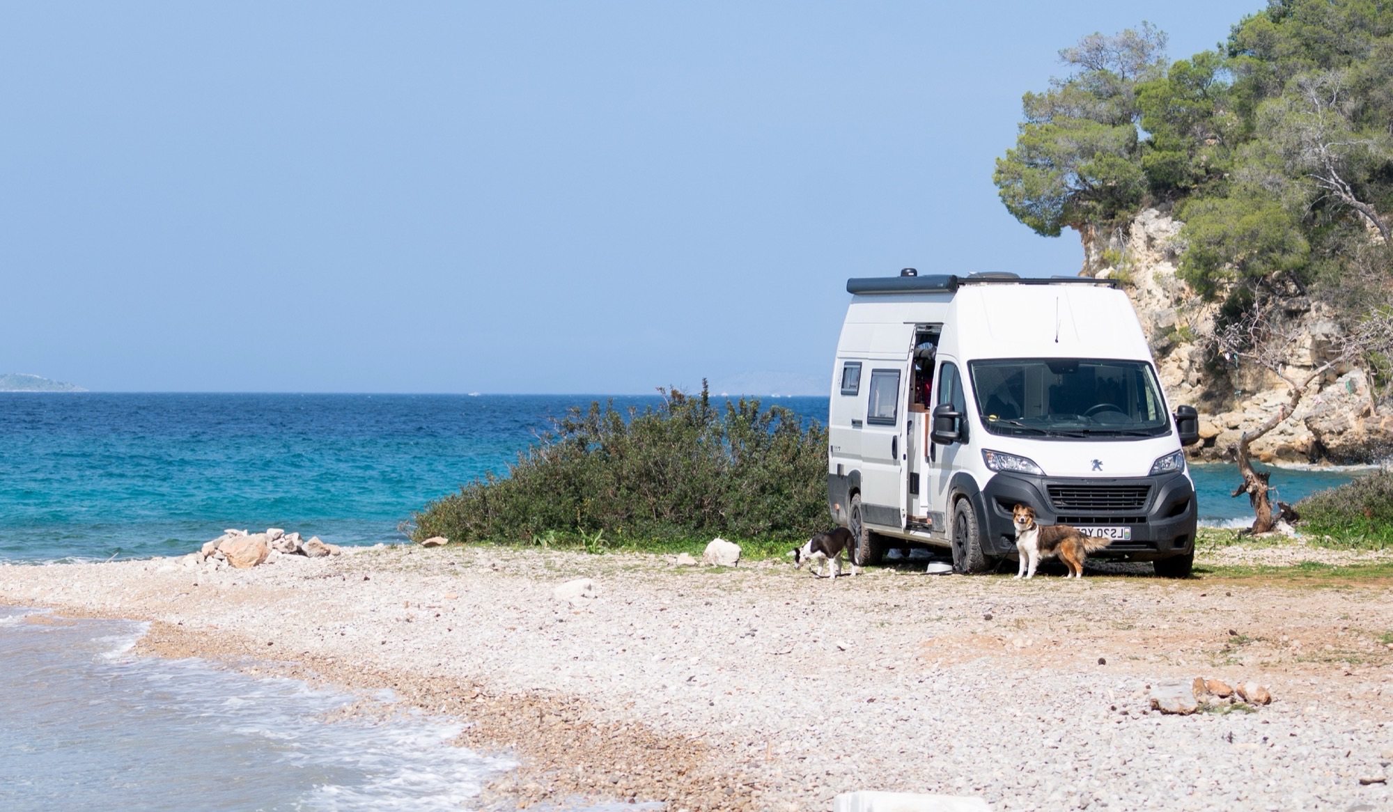 Peugeot Boxer campervan parked on a Mediterranean beach with dogs